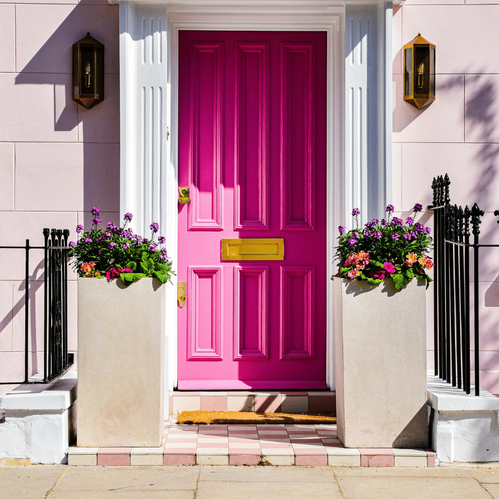 Freshly painted bright pink door with colourful flower planters both sides